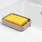 Blim+ Battigia Sponge Holder in taupe holding a yellow sponge beside a sink