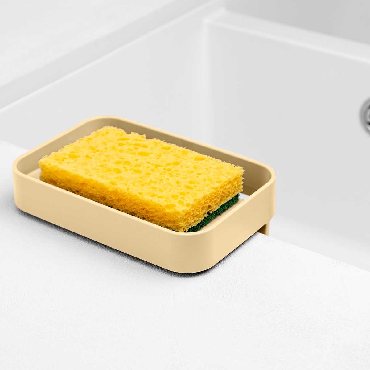 Blim+ Battigia Sponge Holder in cream holding a yellow sponge beside a sink
