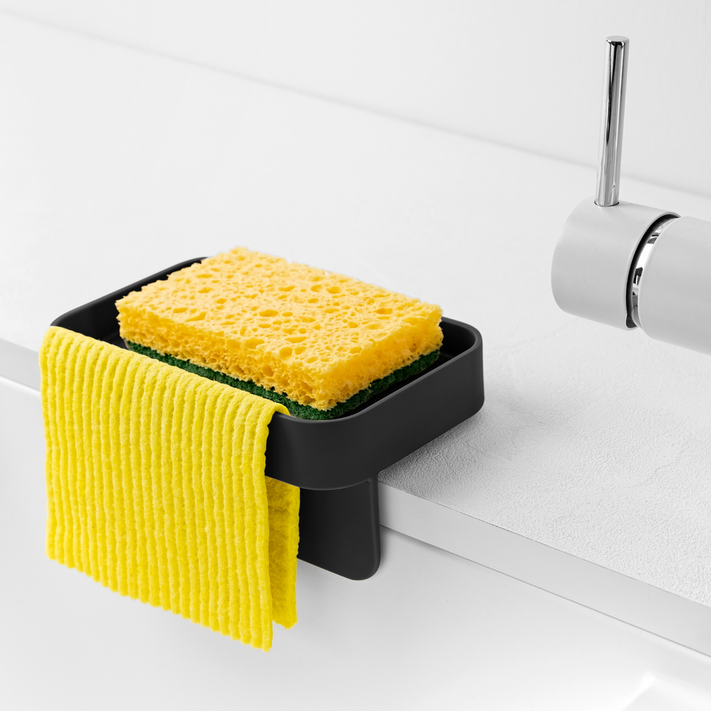 Blim+ Battigia Sponge Holder in black holding a sponge and yellow cloth at a sink