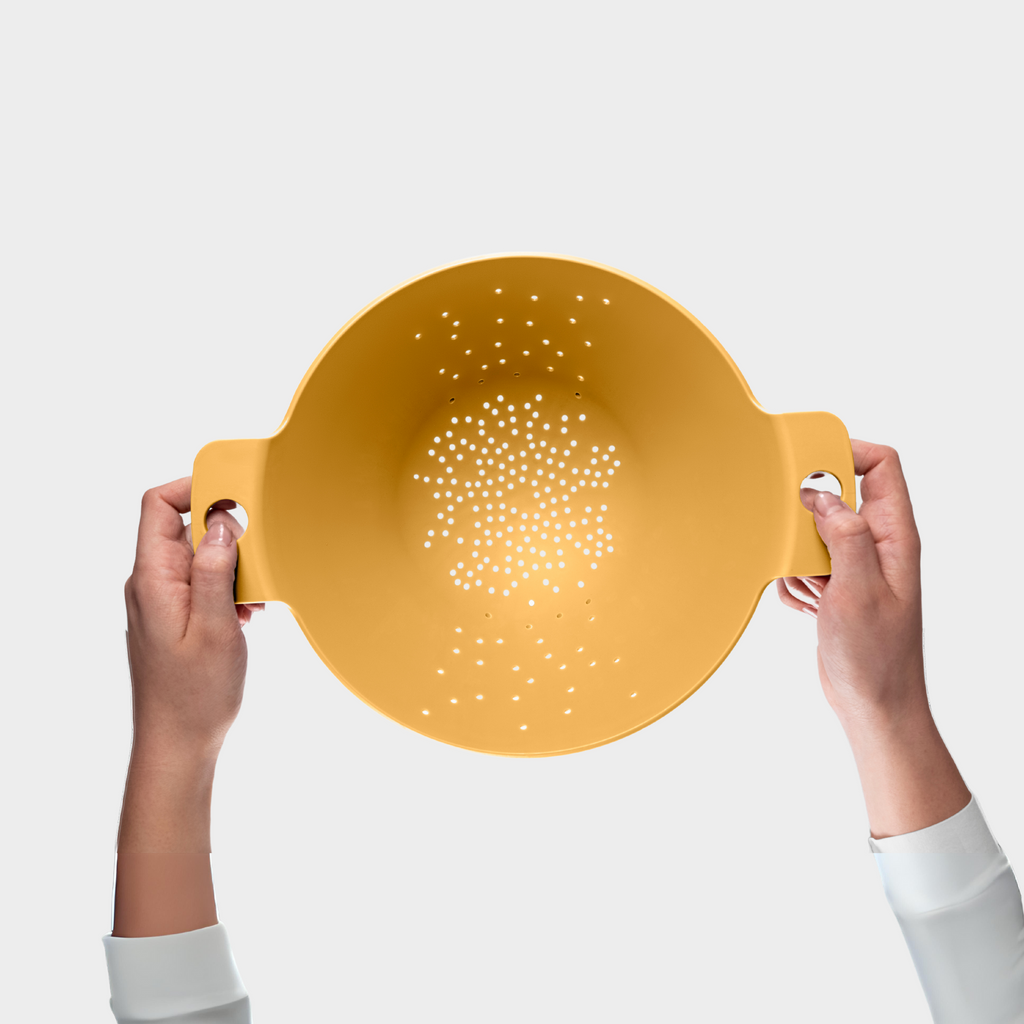 Blim+ Cosmo Colander Medium in yellow, held up in both hands, seen from the front