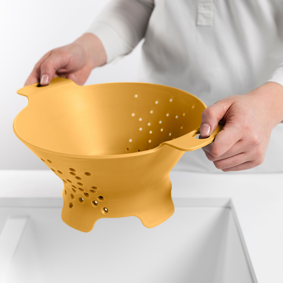 Blim+ Cosmo Colander Medium in yellow, held over a sink
