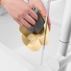 Blim+ Gocciolo Cutlery Drainer in pale yellow, with a hand holding a grey sponge beside a tap