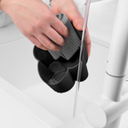 Blim+ Gocciolo Cutlery Drainer in black, with a hand holding a grey sponge beside a tap
