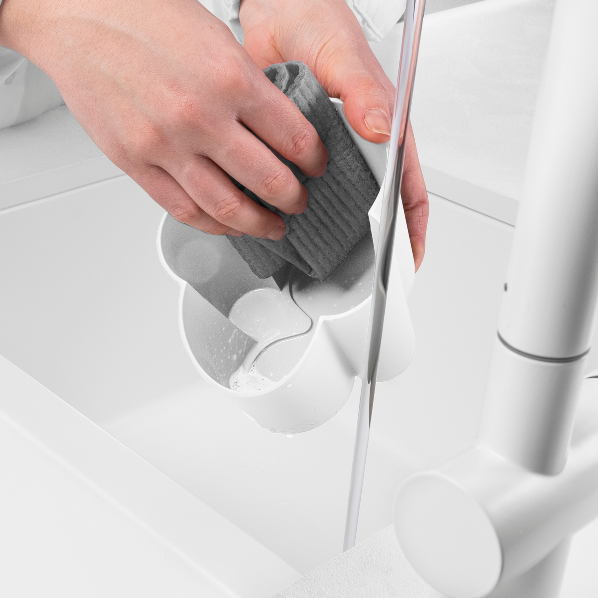 Blim+ Gocciolo Cutlery Drainer in white, with a hand holding a grey sponge beside a tap