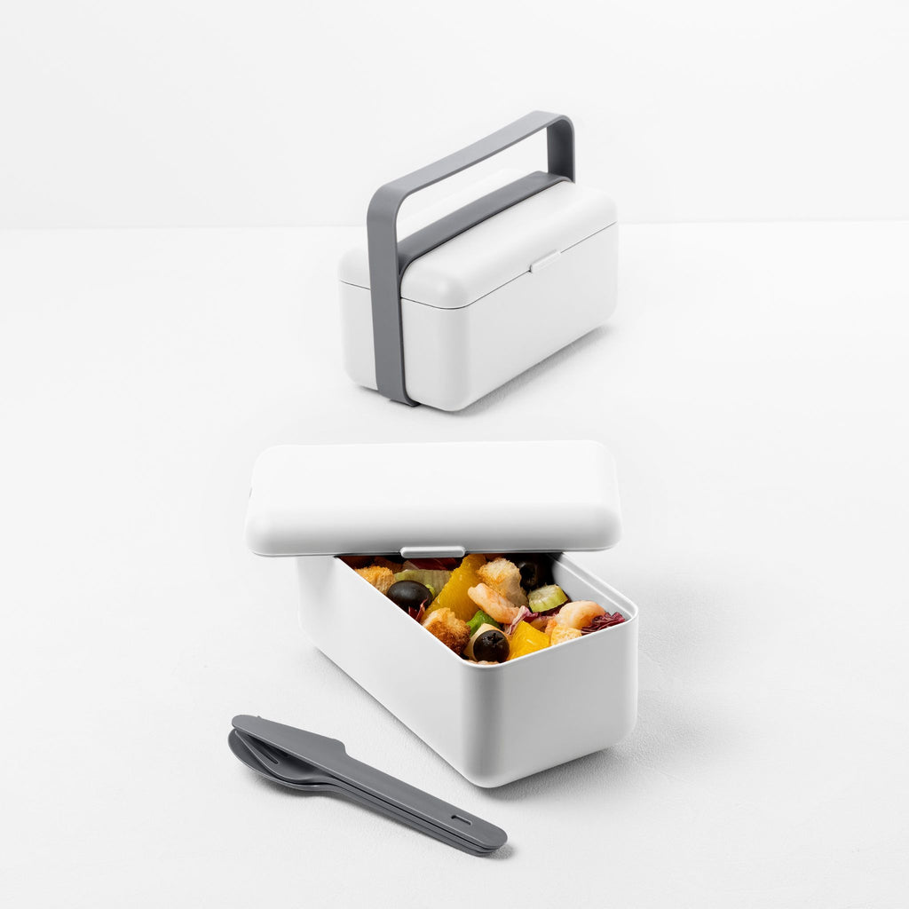 Blim+ Lunchbox Bauletto Small in white with the handle raised, holding snacks, with cutlery