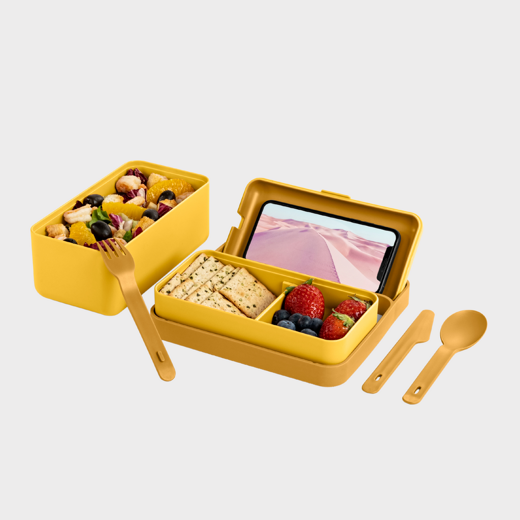 Blim+ Lunchbox Bauletto Medium in yellow, open with a phone, food and cutlery