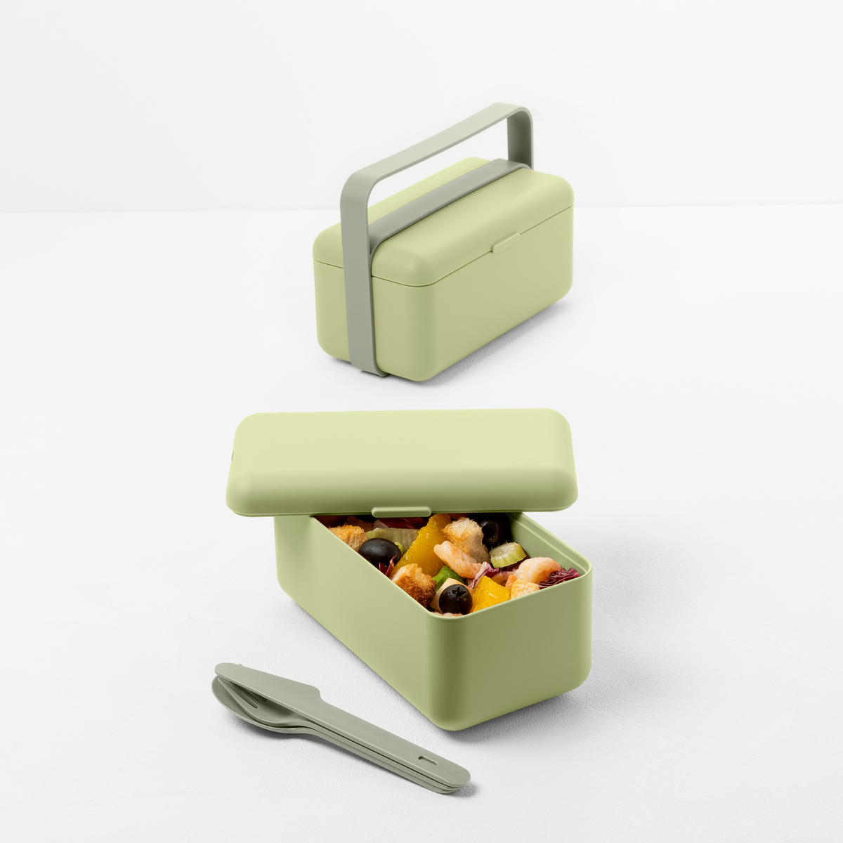 Blim+ Lunchbox Bauletto Small in green with the handle raised, holding snacks, with cutlery