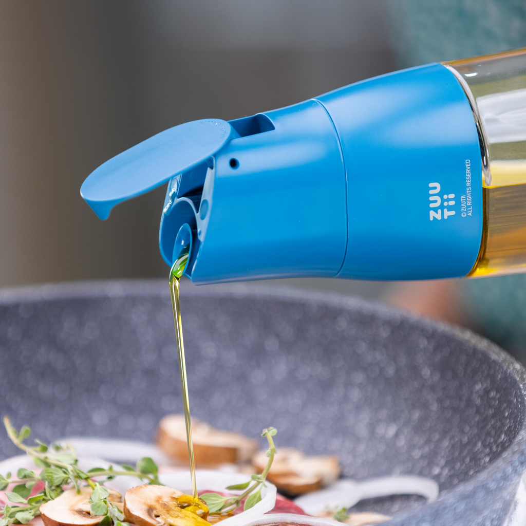 Zuutii Oil Dispenser in blue, pouring oil over food in a pan