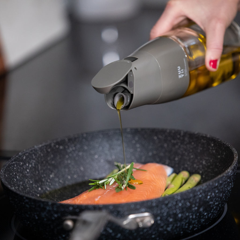 Zuutii Oil Dispenser in dark grey, pouring oil over food in a frying pan