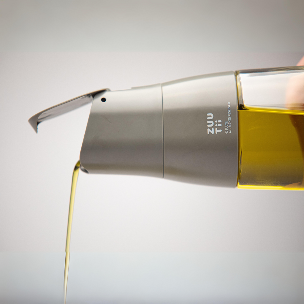 Zuutii Oil Dispenser in dark grey, pouring a thin stream of oil