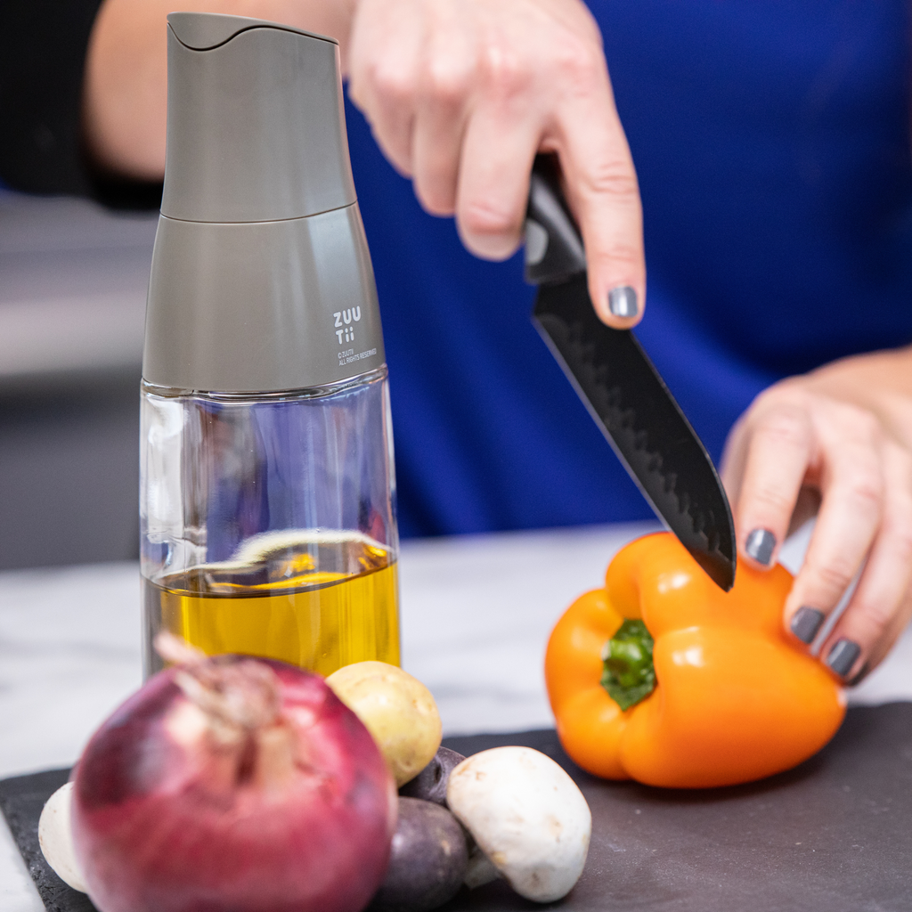 Zuutii Oil Dispenser in dark grey beside a pepper and a red onion on a counter