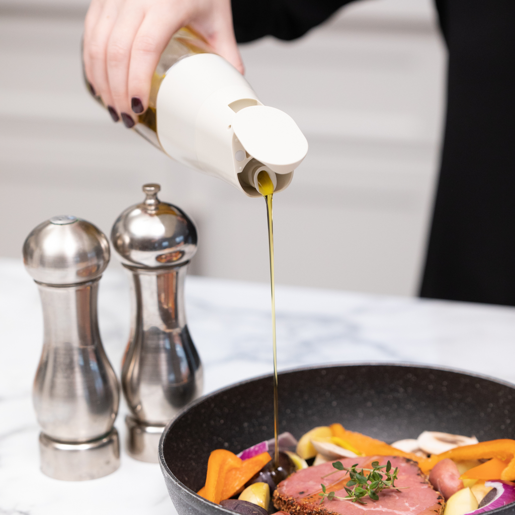 Zuutii Oil Dispenser in cream, pouring oil into a pan beside salt and pepper mills