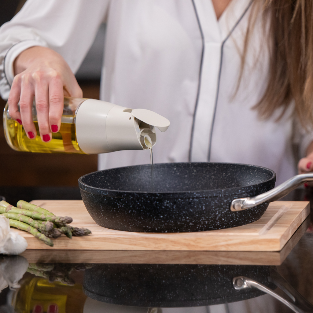 Zuutii Oil Dispenser in cream, pouring oil into a frying pan