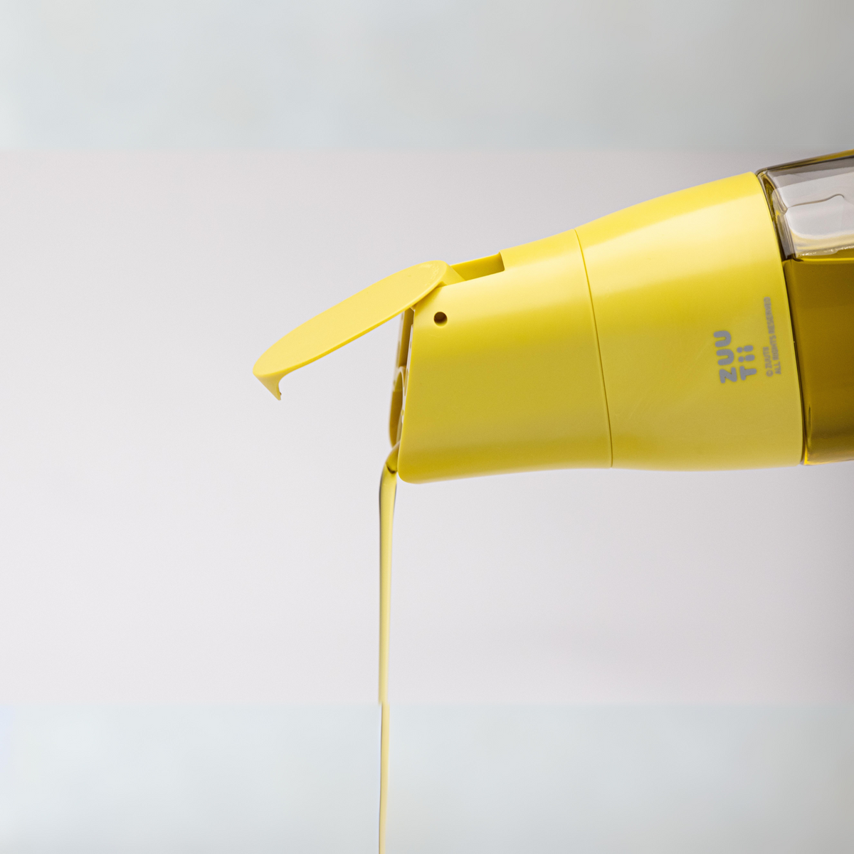 Zuutii Oil Dispenser in yellow, pouring a thin stream of oil