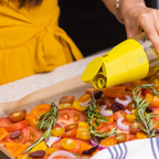 Zuutii Oil Dispenser in yellow, drizzling oil over a tray of roast vegetables
