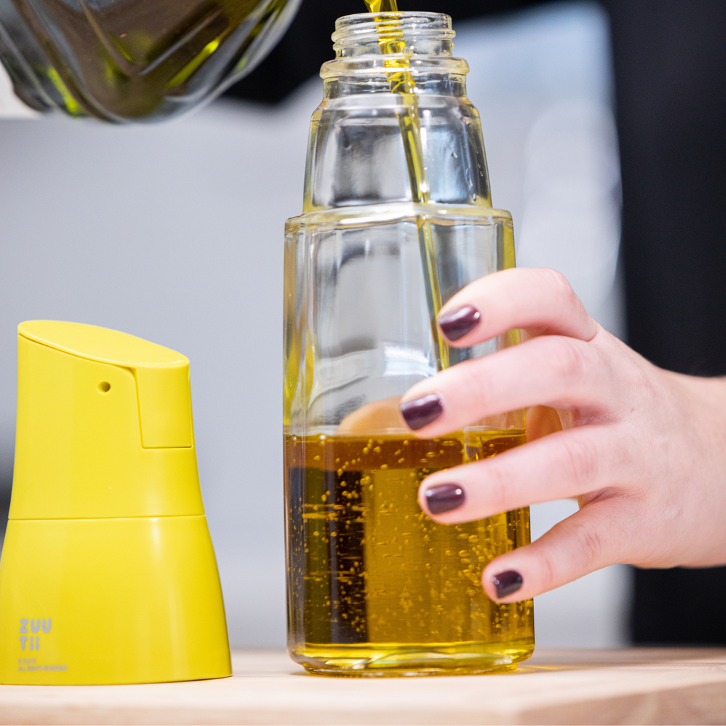 Zuutii Oil Dispenser in yellow, a hand holding the glass base while it is refilled