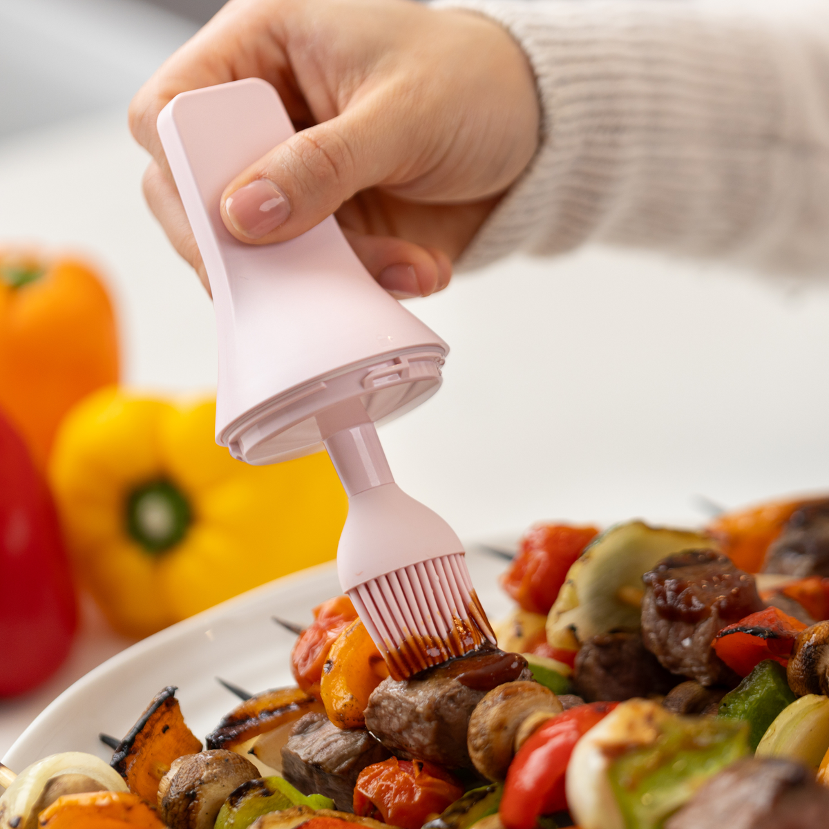 Zuutii Oil Dispenser with Brush in pink, brushing sauce over grilled kebabs