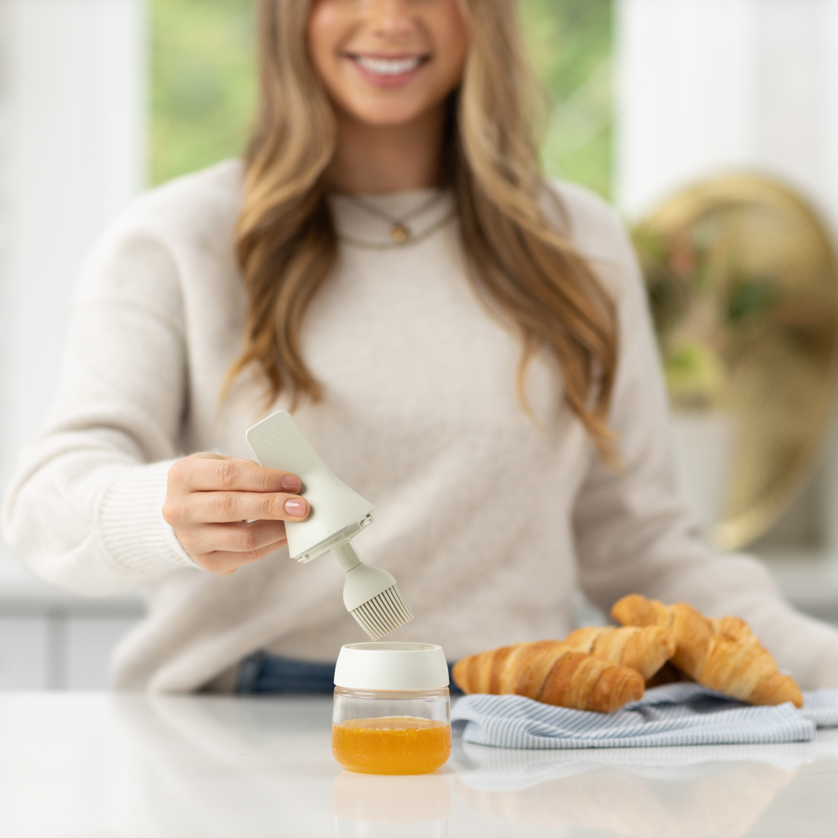 Zuutii Oil Dispenser with Brush in cream, a smiling woman brushing food at a kitchen counter