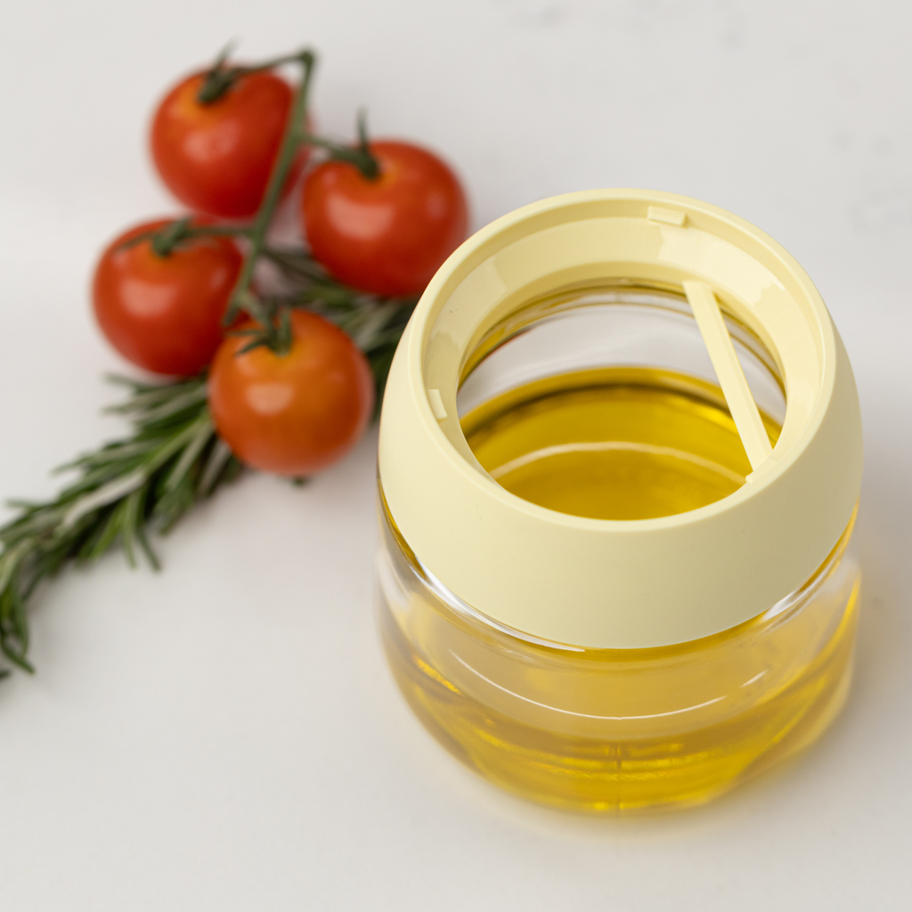 Zuutii Oil Dispenser with Brush in yellow, jar filled with olive oil beside tomatoes and rosemary