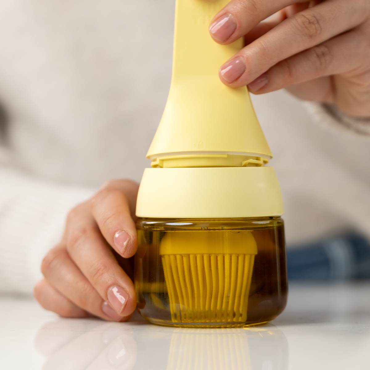 Zuutii Oil Dispenser with Brush in yellow, hands holding the dispenser filled with oil