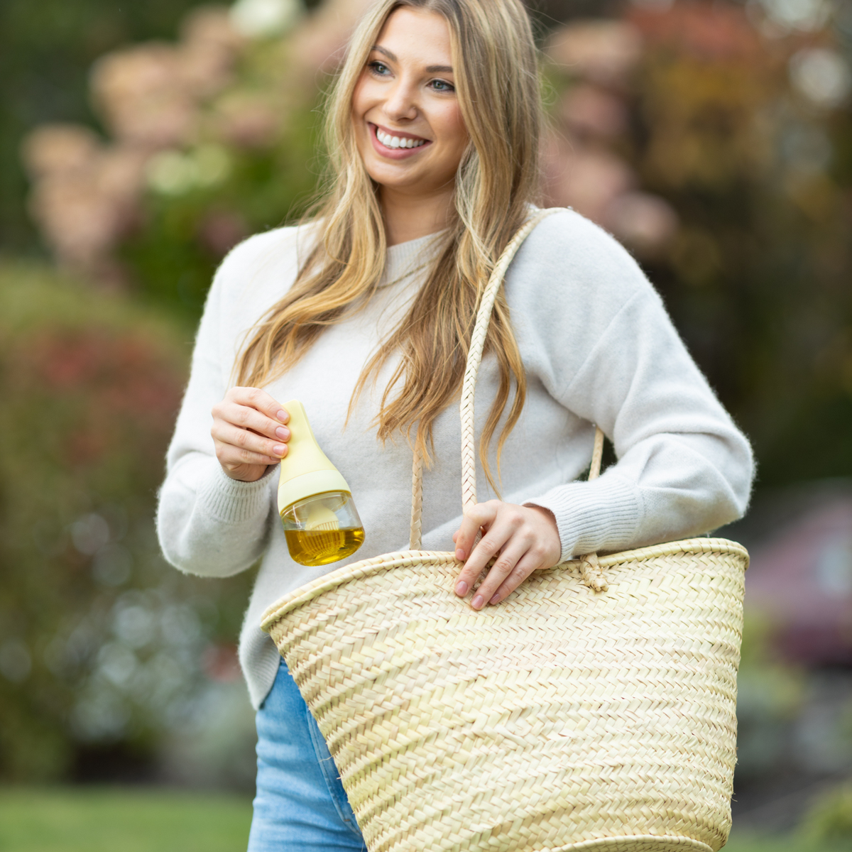 Zuutii Oil Dispenser with Brush in yellow, a smiling woman outdoors holding the dispenser and a basket