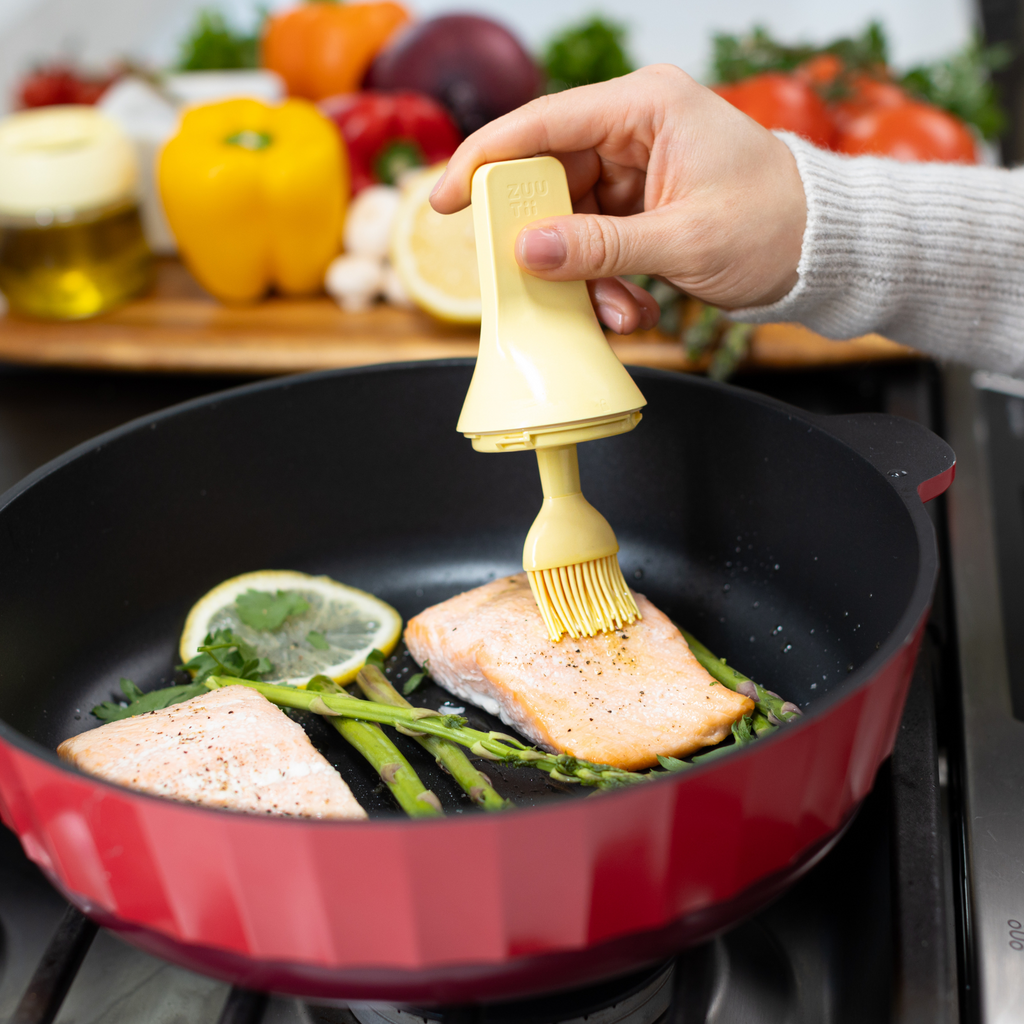 Zuutii Oil Dispenser with Brush in yellow, brushing oil on salmon in a red pan