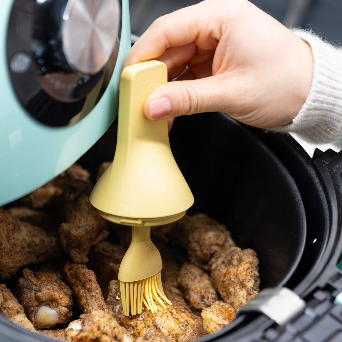 Zuutii Oil Dispenser with Brush in yellow, brushing oil over cooked food in a black dish