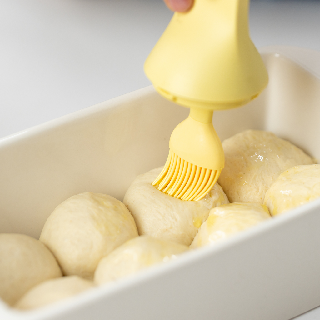 Zuutii Oil Dispenser with Brush in yellow, brushing oil over dough balls in a baking dish