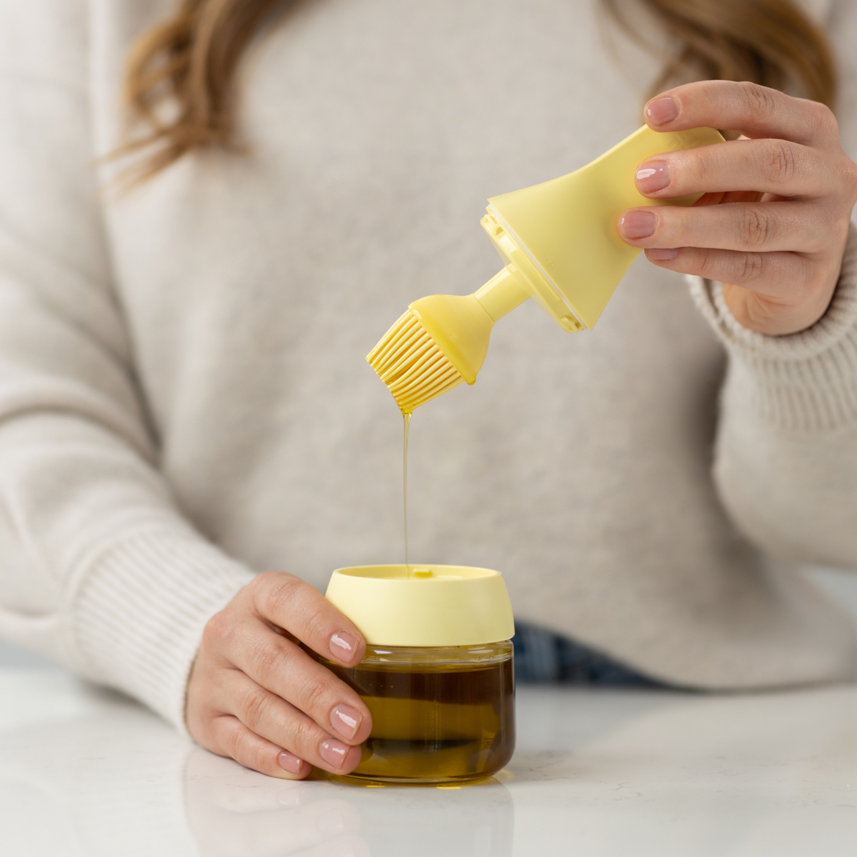 Zuutii Oil Dispenser with Brush in yellow, a woman dipping the brush into the jar