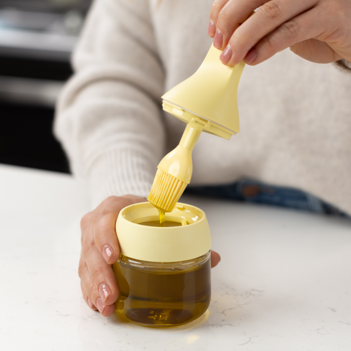Zuutii Oil Dispenser with Brush in yellow, a person lifting the brush out of the jar