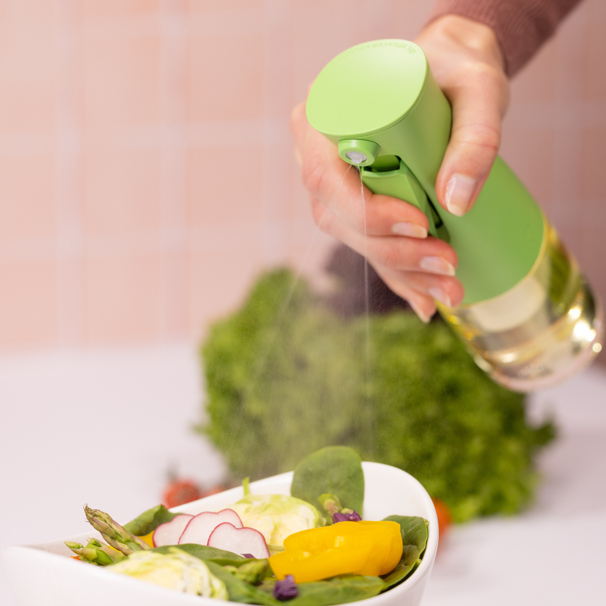 Zuutii Oil Sprayer in green, spraying oil over a salad