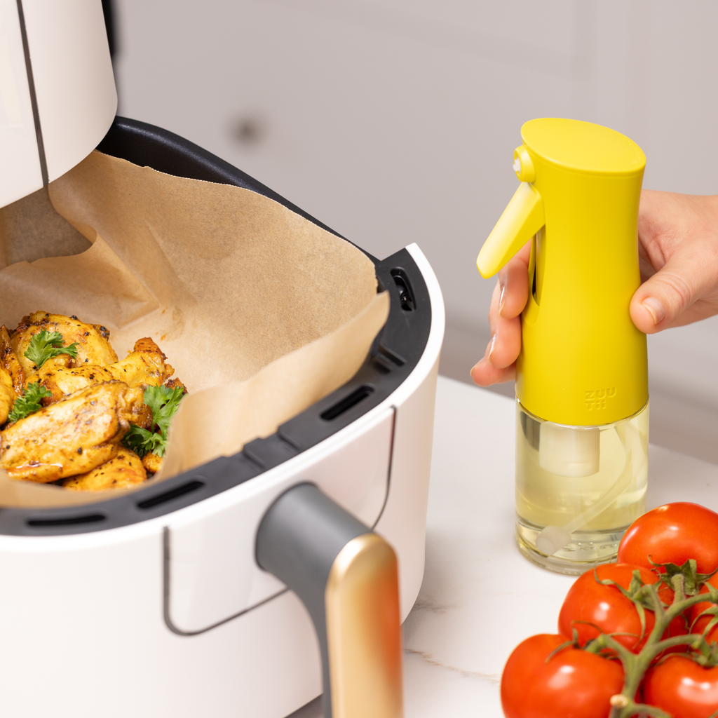 Zuutii Oil Sprayer in yellow beside a cooking basket of roast chicken