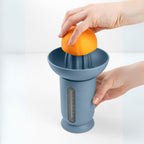 Blim+ UFO Juicer with QB Carafe in blue, with an orange being juiced by hand