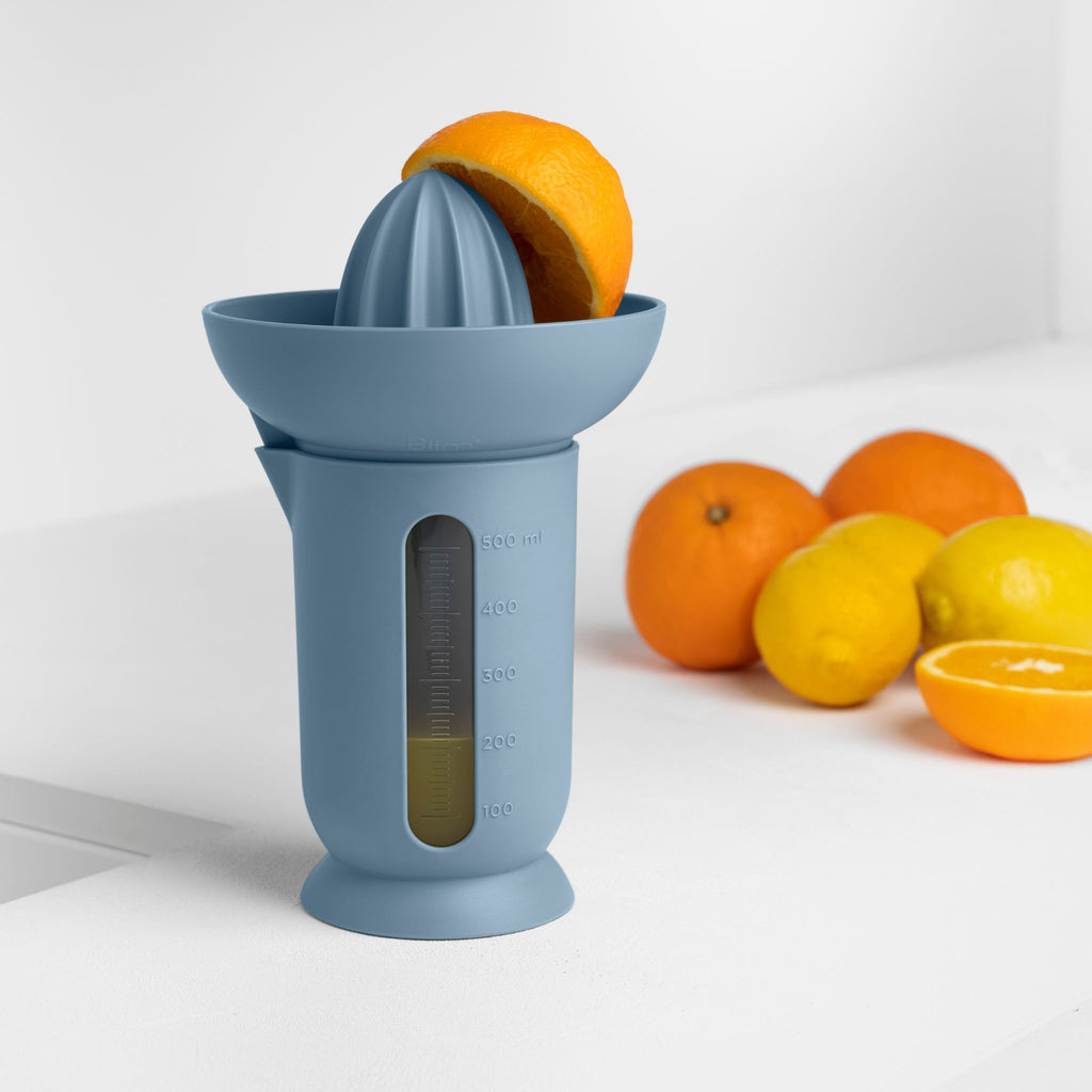 Blim+ UFO Juicer with QB Carafe in blue, beside fresh oranges