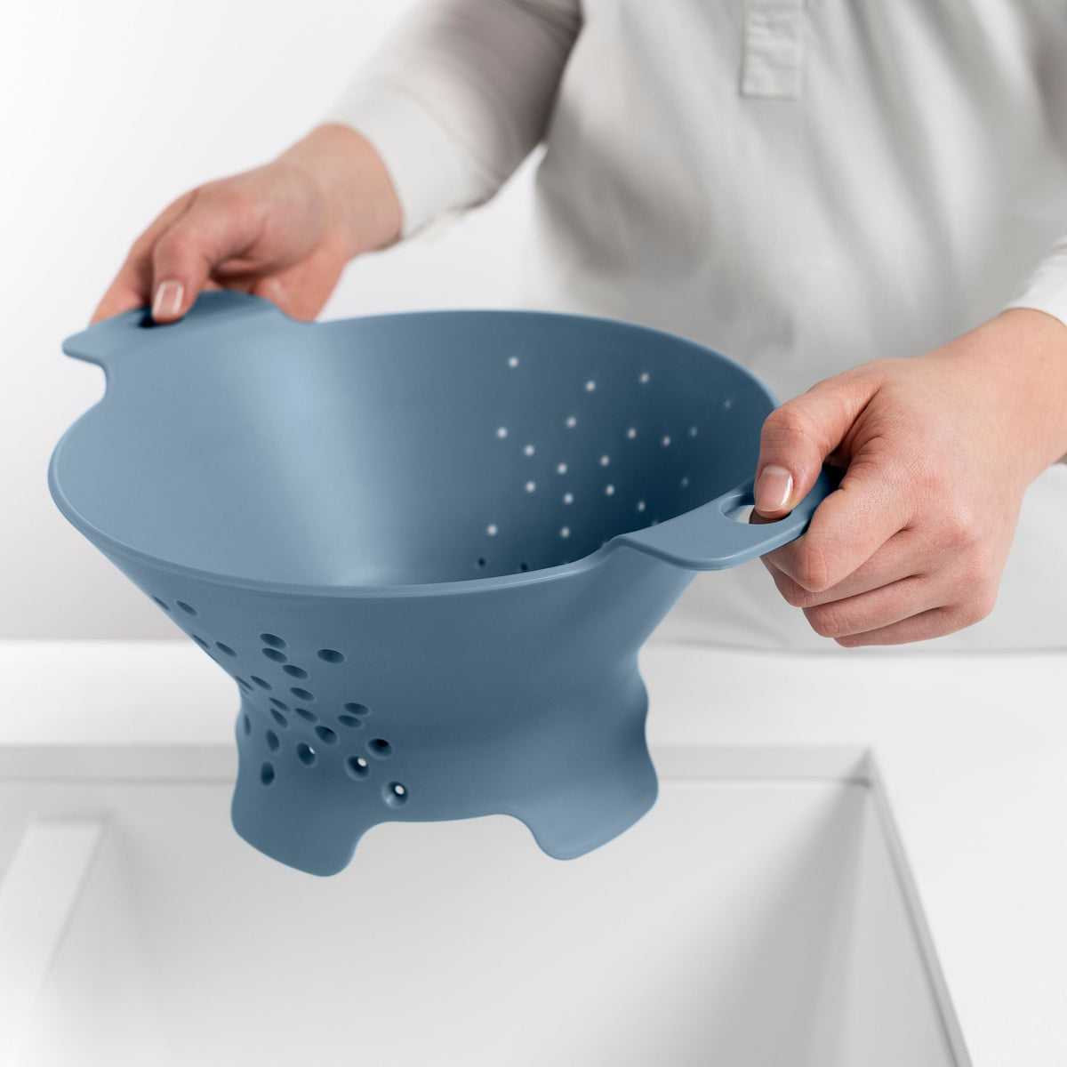 Blim+ Cosmo Colander Medium in blue, held over a sink