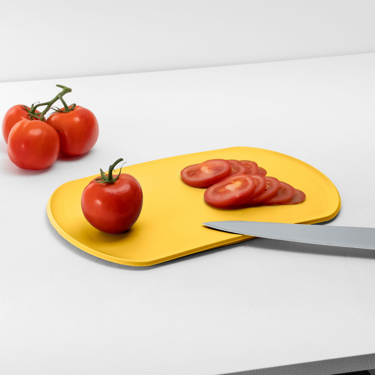 Blim+ Skateboard Chopping Board Medium in yellow, with sliced tomatoes and a knife