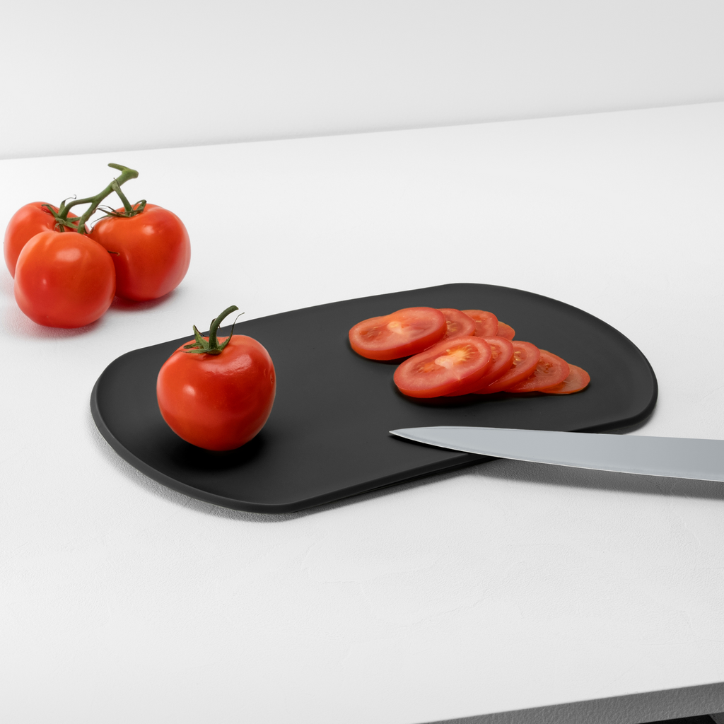 Blim+ Skateboard Chopping Board Medium in black, with sliced tomatoes and a knife