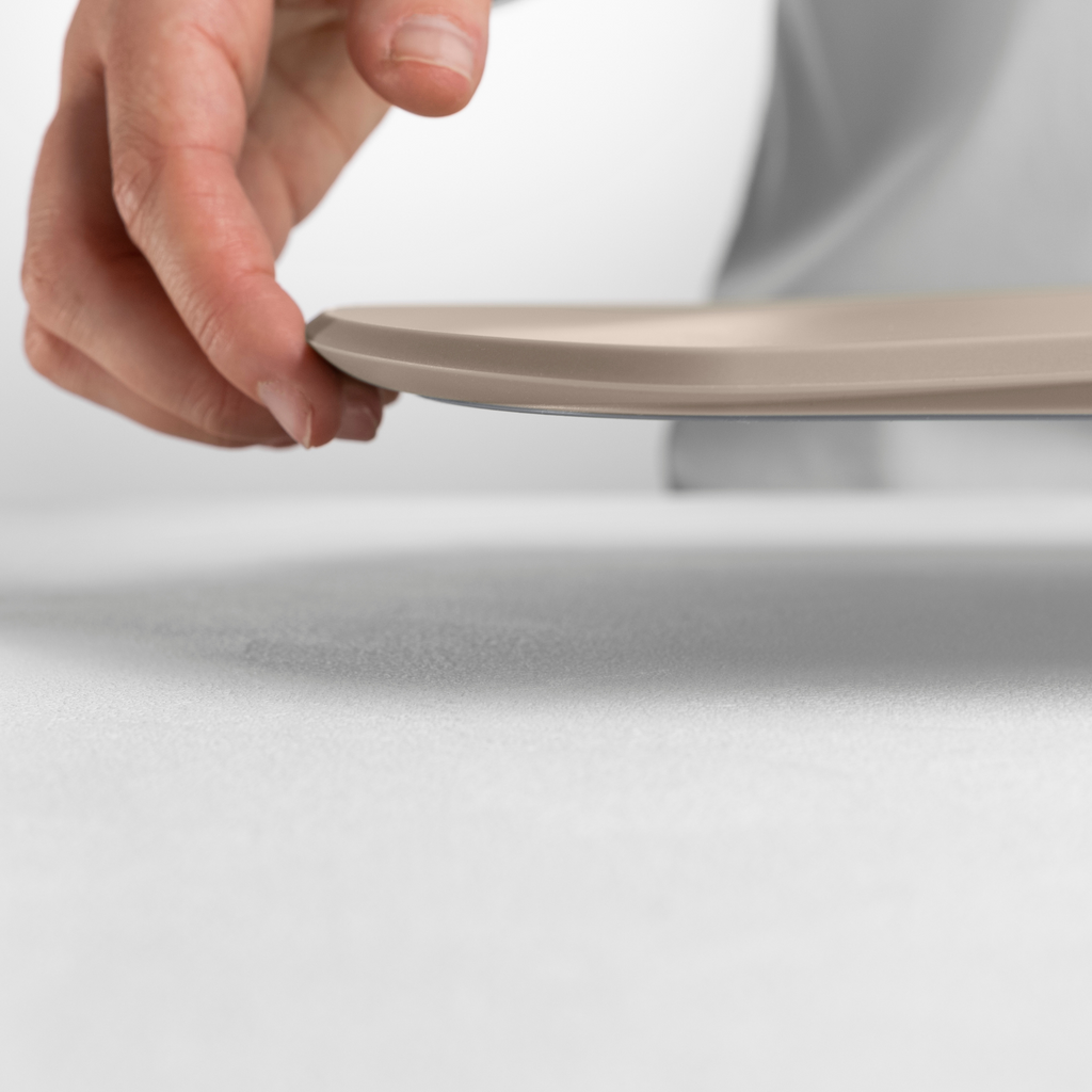 Blim+ Skateboard Chopping Board Medium in taupe, lifted by hand to show its thin profile