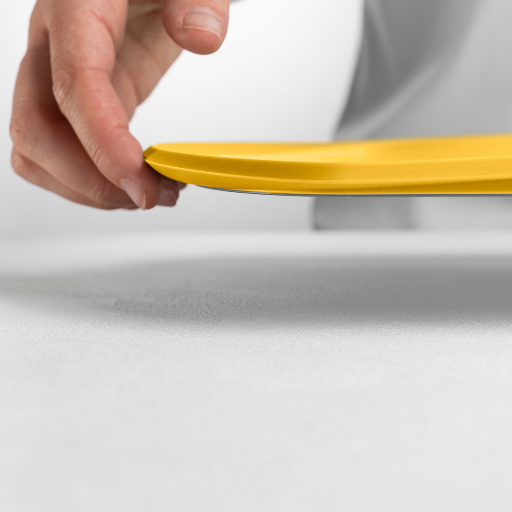 Blim+ Skateboard Chopping Board Medium in yellow, lifted by hand to show its thin profile