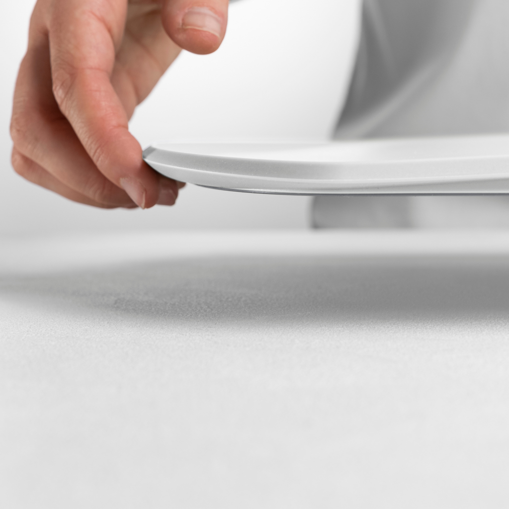 Blim+ Skateboard Chopping Board Medium in white, lifted by hand to show its thin profile