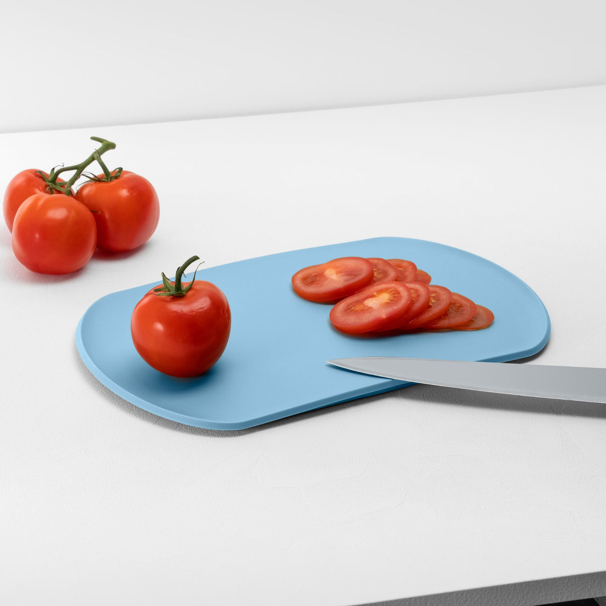 Blim+ Skateboard Chopping Board Medium in blue, with sliced tomatoes and a knife