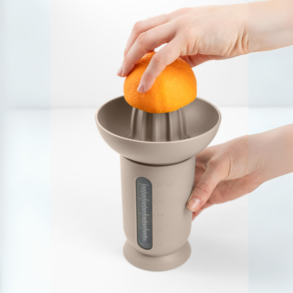 Blim+ UFO Juicer with QB Carafe in taupe, with an orange being juiced by hand