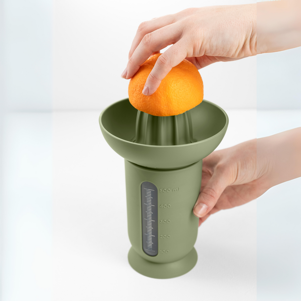 Blim+ UFO Juicer with QB Carafe in green, with an orange being juiced by hand
