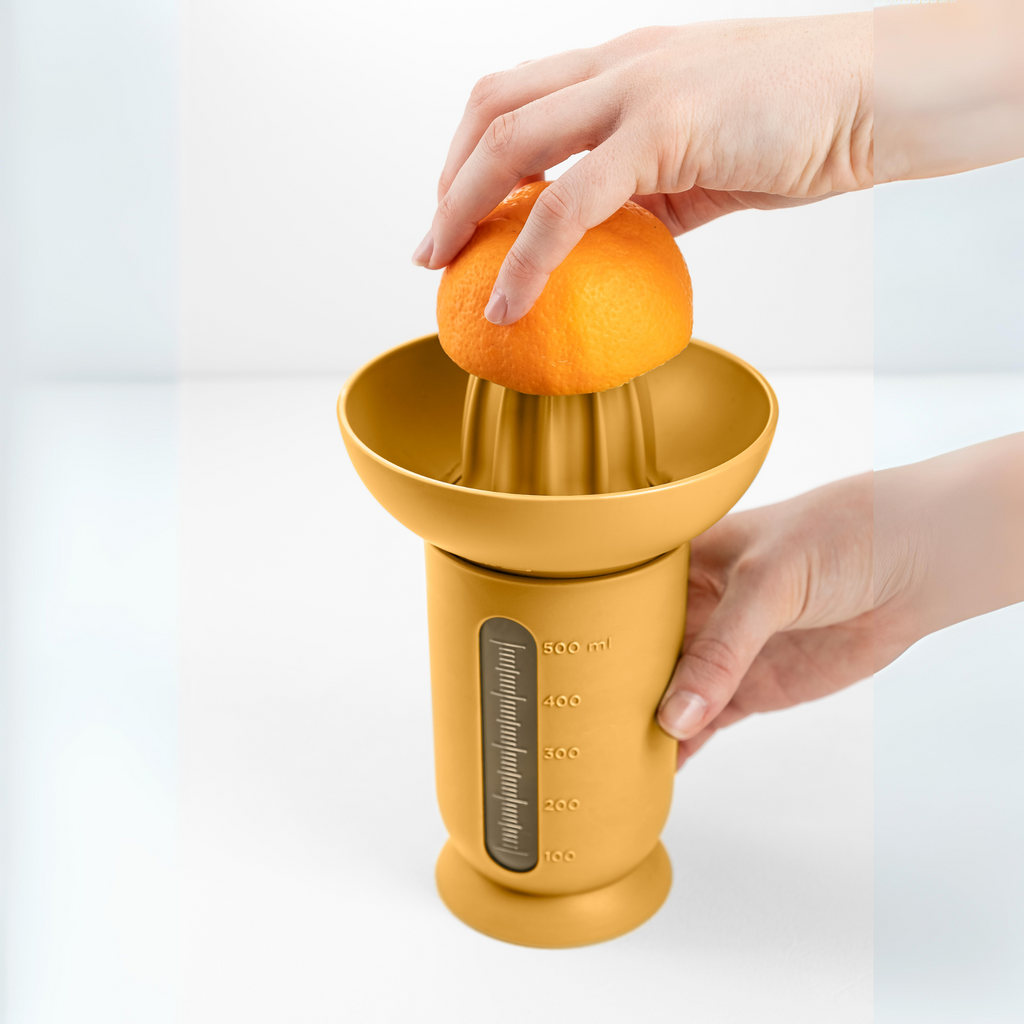 Blim+ UFO Juicer with QB Carafe in yellow, with an orange being juiced by hand