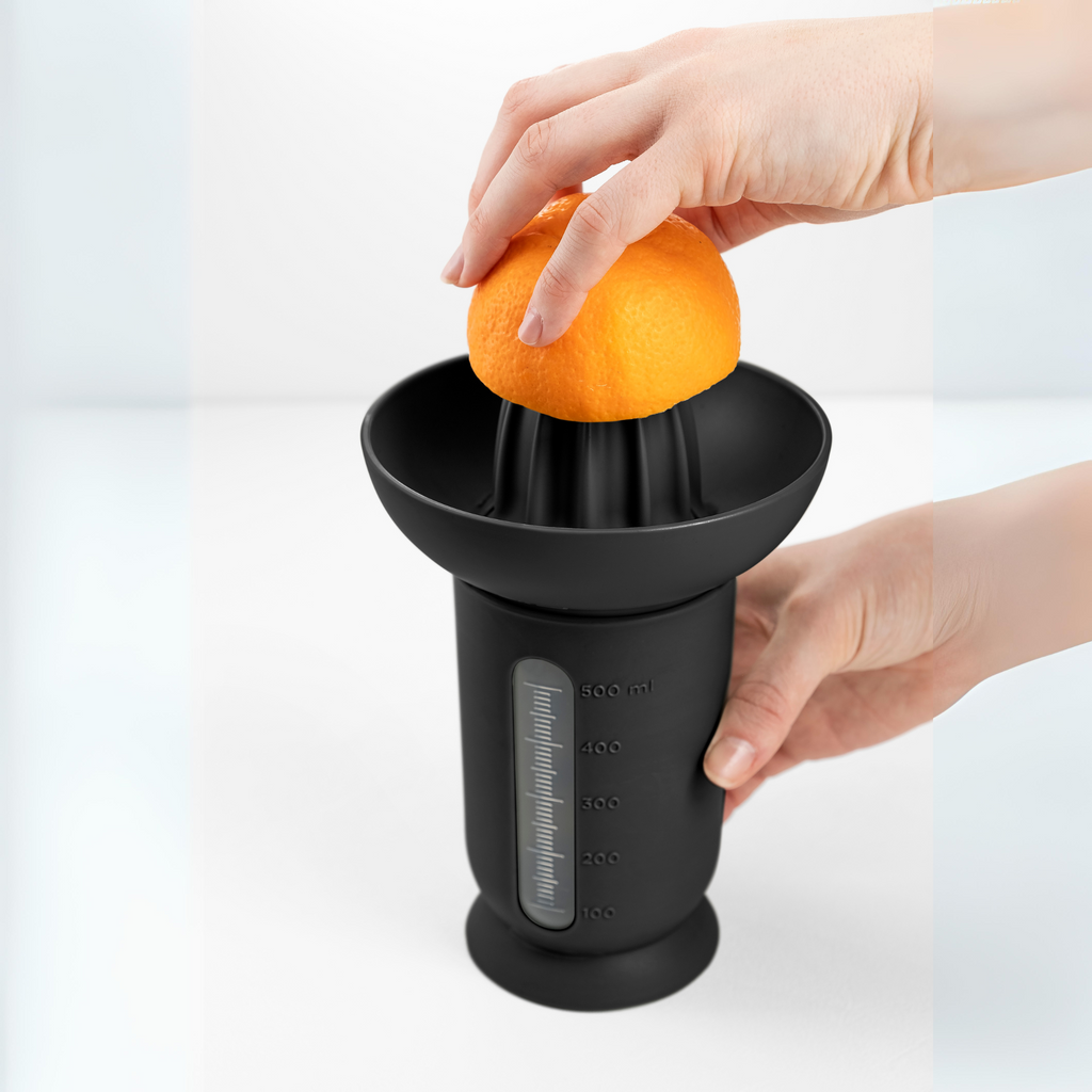 Blim+ UFO Juicer with QB Carafe in black, with an orange being juiced by hand
