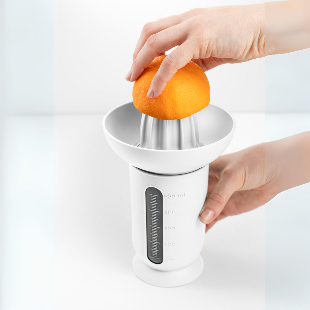 Blim+ UFO Juicer with QB Carafe in white, with an orange being juiced by hand