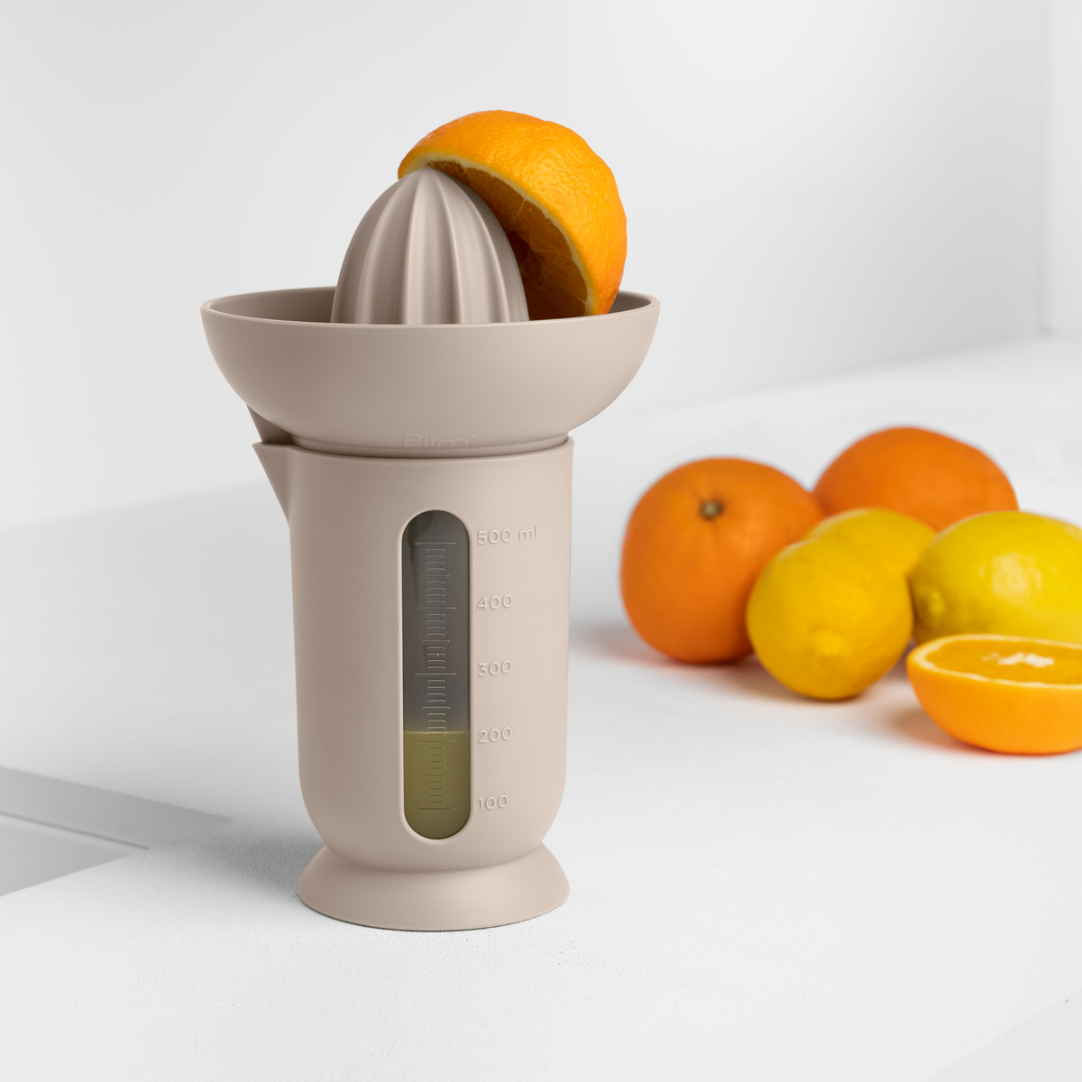 Blim+ UFO Juicer with QB Carafe in taupe, beside fresh oranges