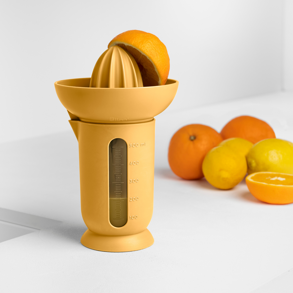 Blim+ UFO Juicer with QB Carafe in yellow, beside fresh oranges