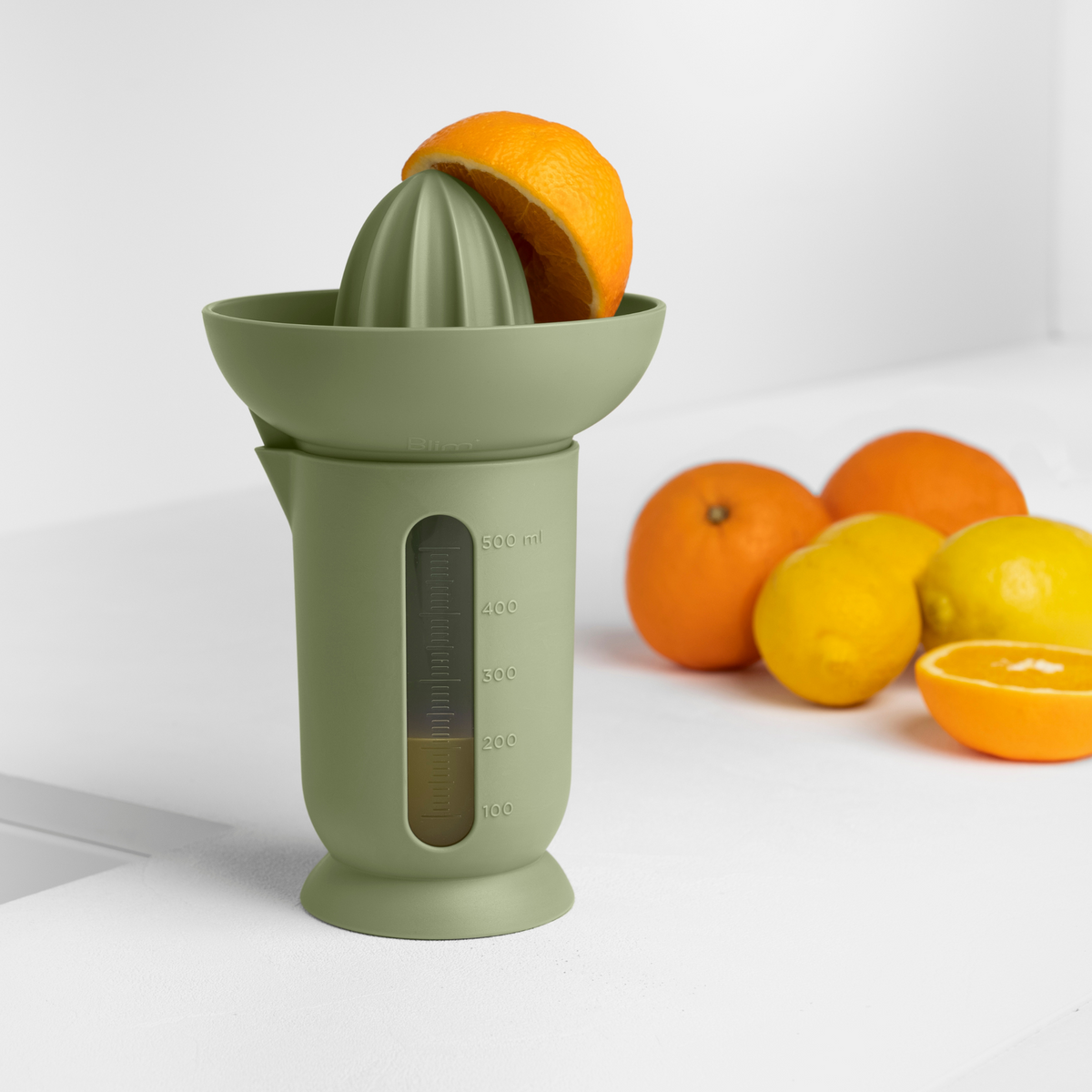 Blim+ UFO Juicer with QB Carafe in green, beside fresh oranges