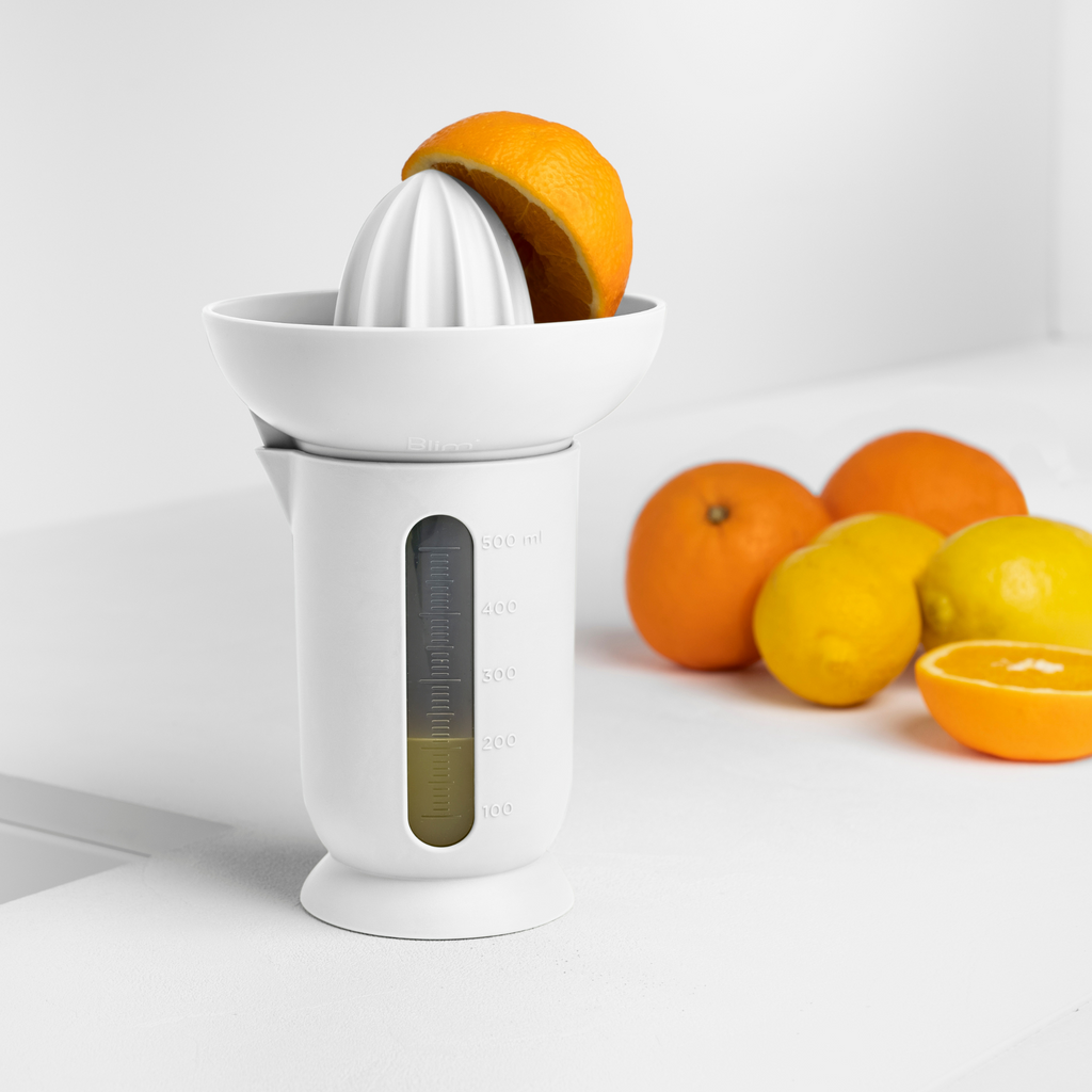 Blim+ UFO Juicer with QB Carafe in white, beside fresh oranges